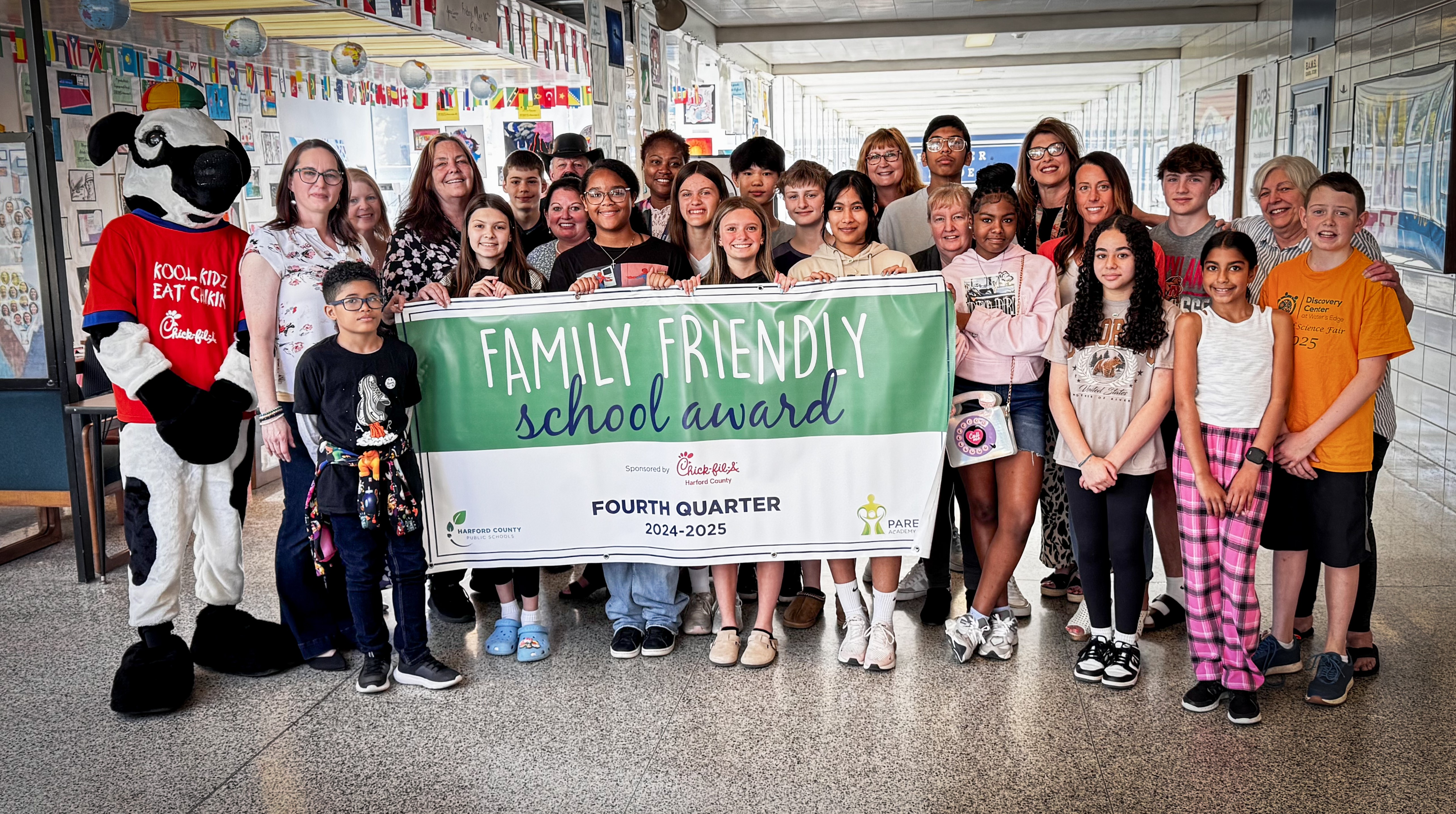 School system leaders, students, and Chick-fil-A mascot hold up Fourth Quarter Family Friendly School Award banner.